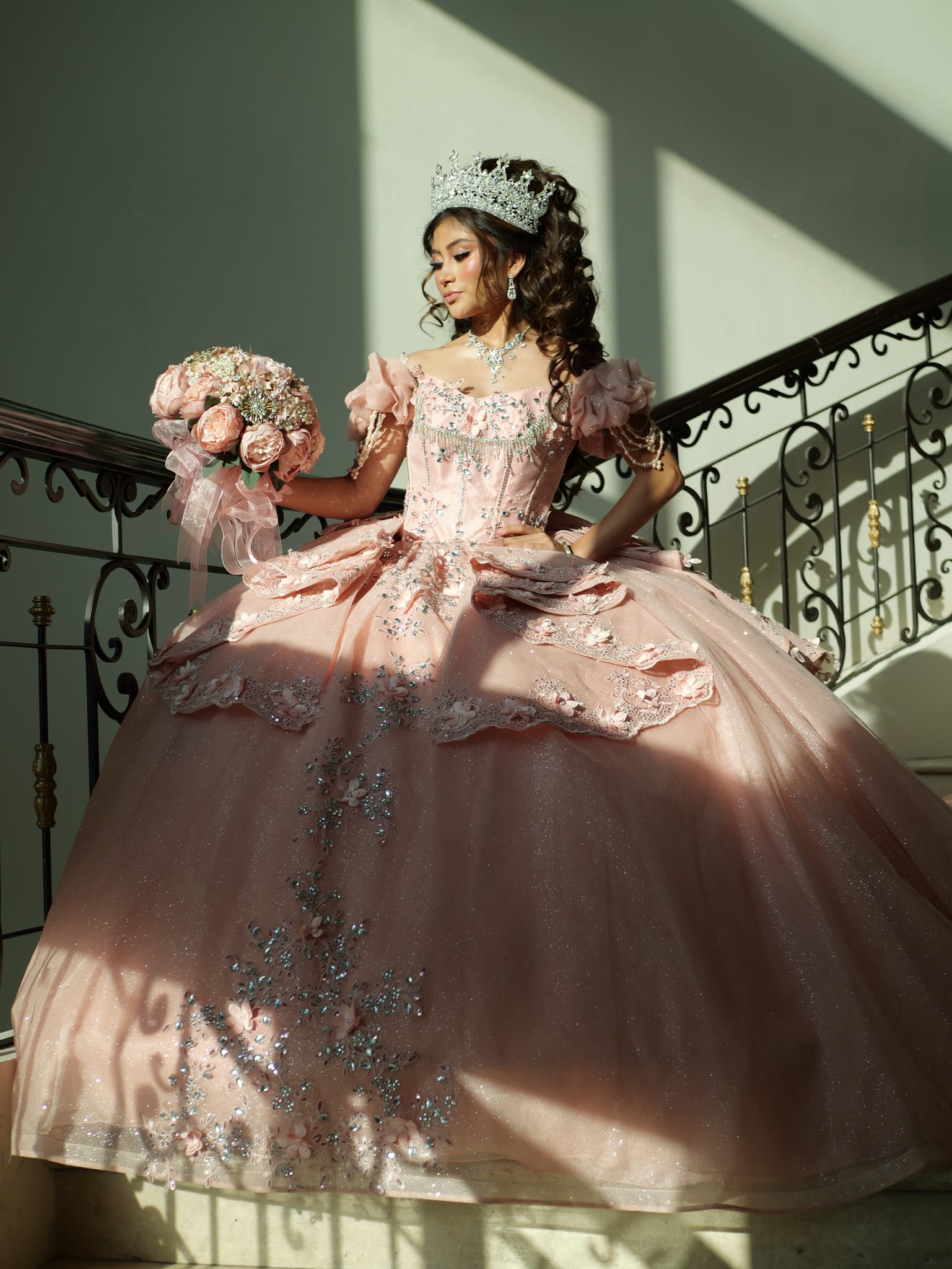 Quinceañera con vestido rosa empolvado en una escalera de hierro forjado